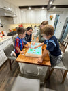 A family of three kids and one adult gather around a kitchen island to play the Board console, using their hands and playing pieces to interact with the screen.